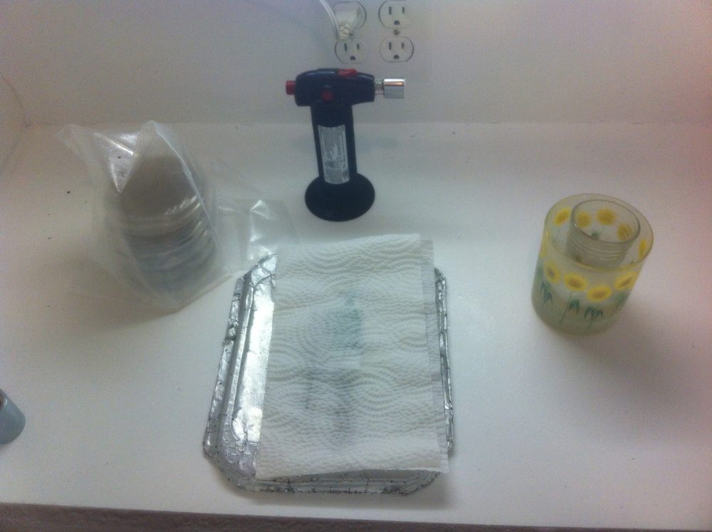 Glove box set up for cloning. Agar plates (with antibiotic if possible, this is plain) and cello-sealing tape, butane torch, scapel, and CotW sample in H2O2. Wash the air with bleach water.